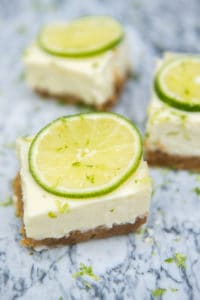 3 key lime pie bars on a marble slab topped with lime slices and lime zest